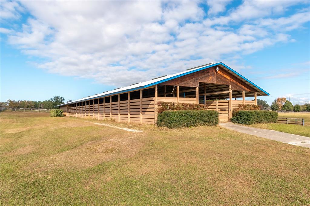 A long, single-story wooden horse barn with a blue-trimmed metal roof sits on grass — 5100 W HWY 329, REDDICK, FL