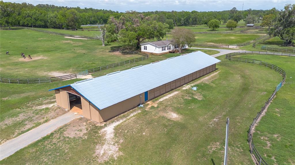 An aerial view of a long metal-roofed barn situated on a fenced horse farm — 5100 W HWY 329, REDDICK, FL