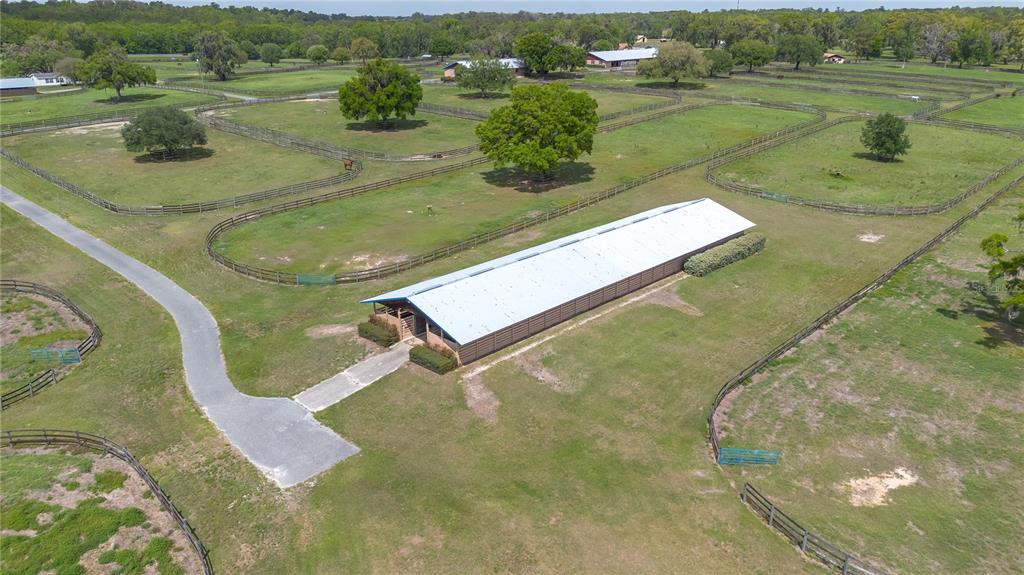 An aerial view shows a long, metal-roofed barn surrounded by fenced pastures and mature trees — 5100 W HWY 329, REDDICK, FL