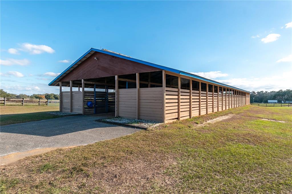 A long, open-air wooden horse stable with a metal roof stands on a grassy lot — 5100 W HWY 329, REDDICK, FL