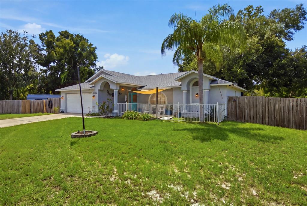 A single-story house with a white fence, a palm tree, and a tan shade sail — 13801 WHITBY ROAD, HUDSON, FL