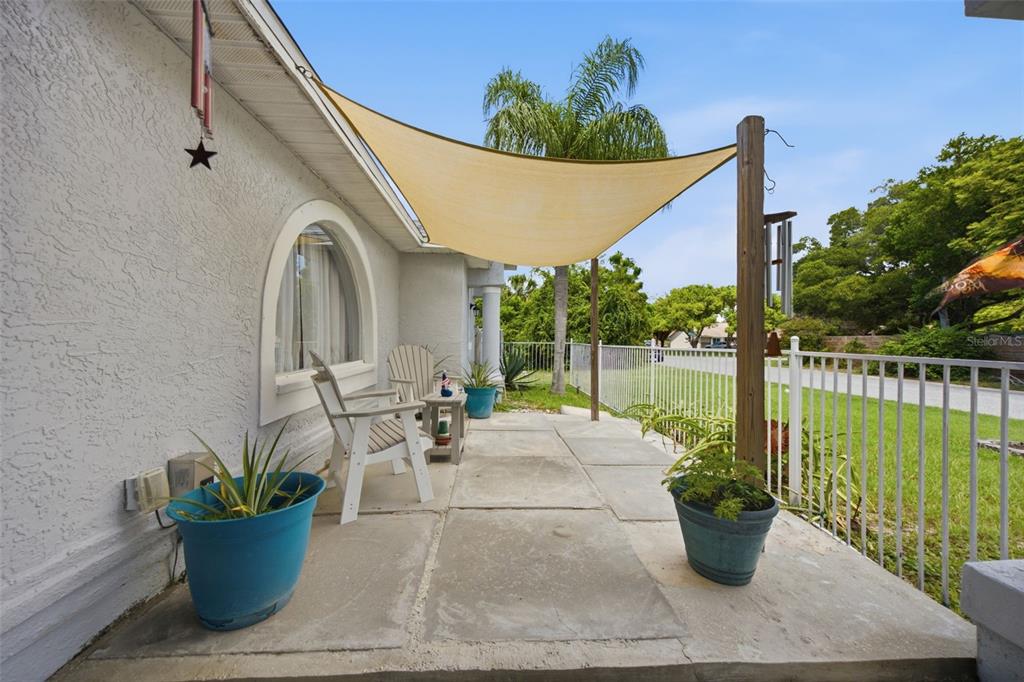 A concrete patio features a tan shade sail, white chairs, and potted plants — 13801 WHITBY ROAD, HUDSON, FL
