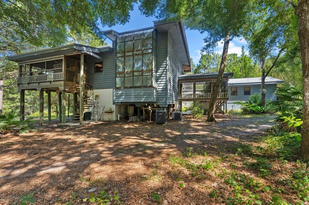 A two-story house on stilts features a large glass window wall and a screened porch — 400 PINE BLUFF TRAIL, ORMOND BEACH, FL