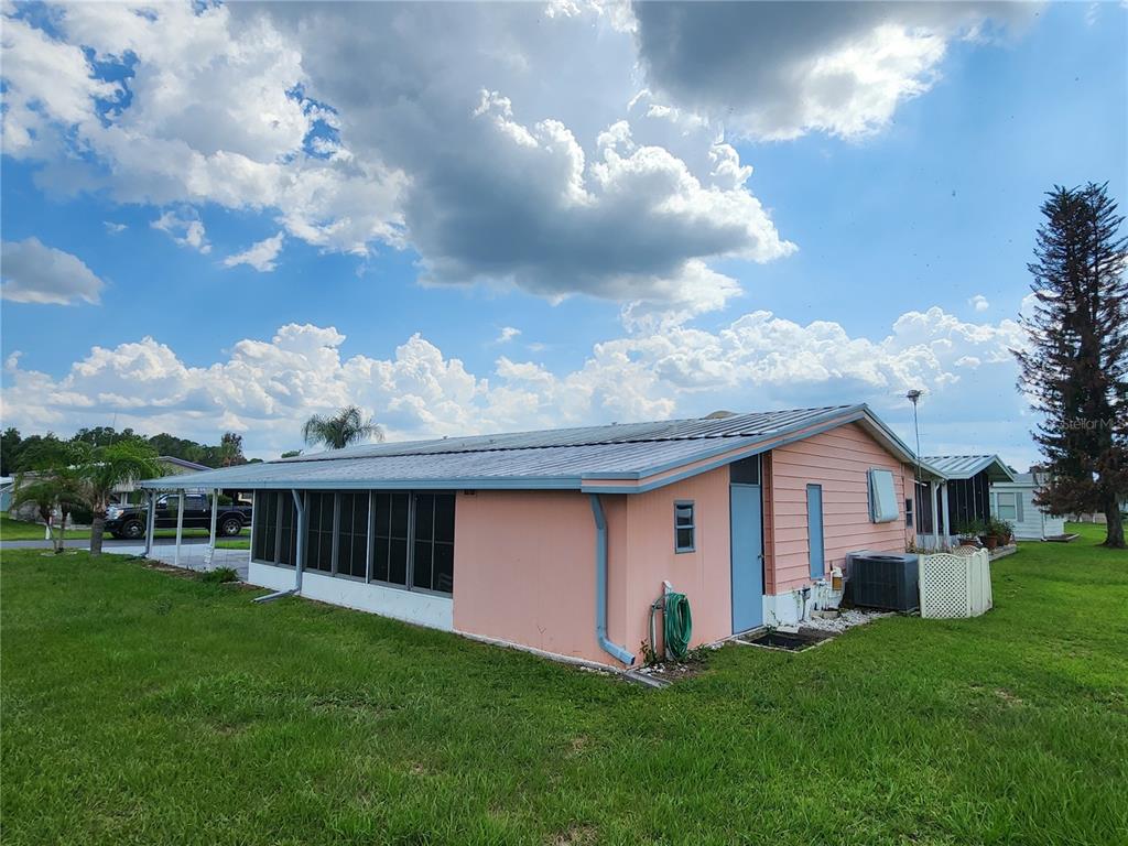 A pink mobile home with a metal roof and a screened-in porch sits on grass — 113 LAKE HAZEL DRIVE, WINTER HAVEN, FL