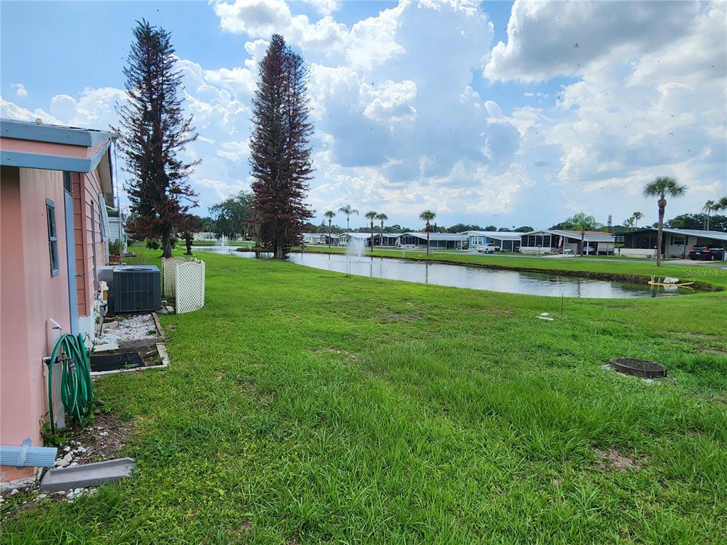 A view of a grassy backyard with a pond, fountain, and neighboring mobile homes — 113 LAKE HAZEL DRIVE, WINTER HAVEN, FL