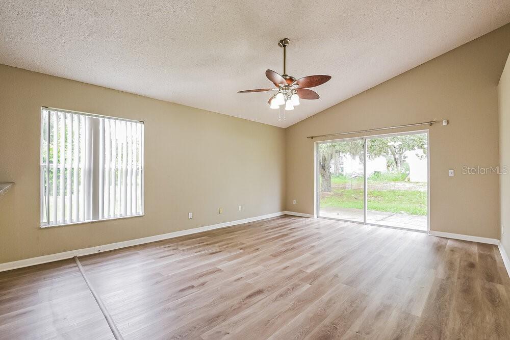 An empty living room features light wood-look flooring, a vaulted ceiling, and sliding glass doors — 3005 LORIMER COURT, GROVELAND, FL