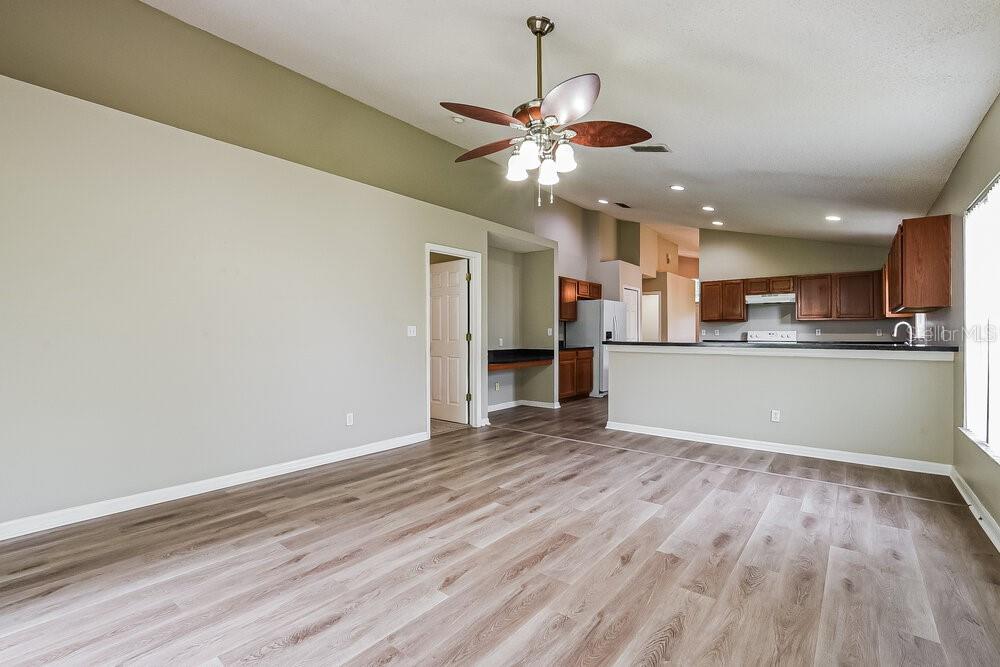 A living room with light-colored walls, wood-look flooring, a ceiling fan, and an open kitchen — 3005 LORIMER COURT, GROVELAND, FL