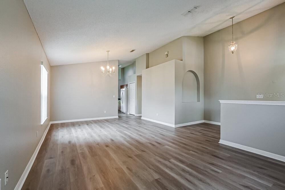 An empty room with light gray walls, wood-look flooring, a vaulted ceiling, and two chandeliers — 3005 LORIMER COURT, GROVELAND, FL