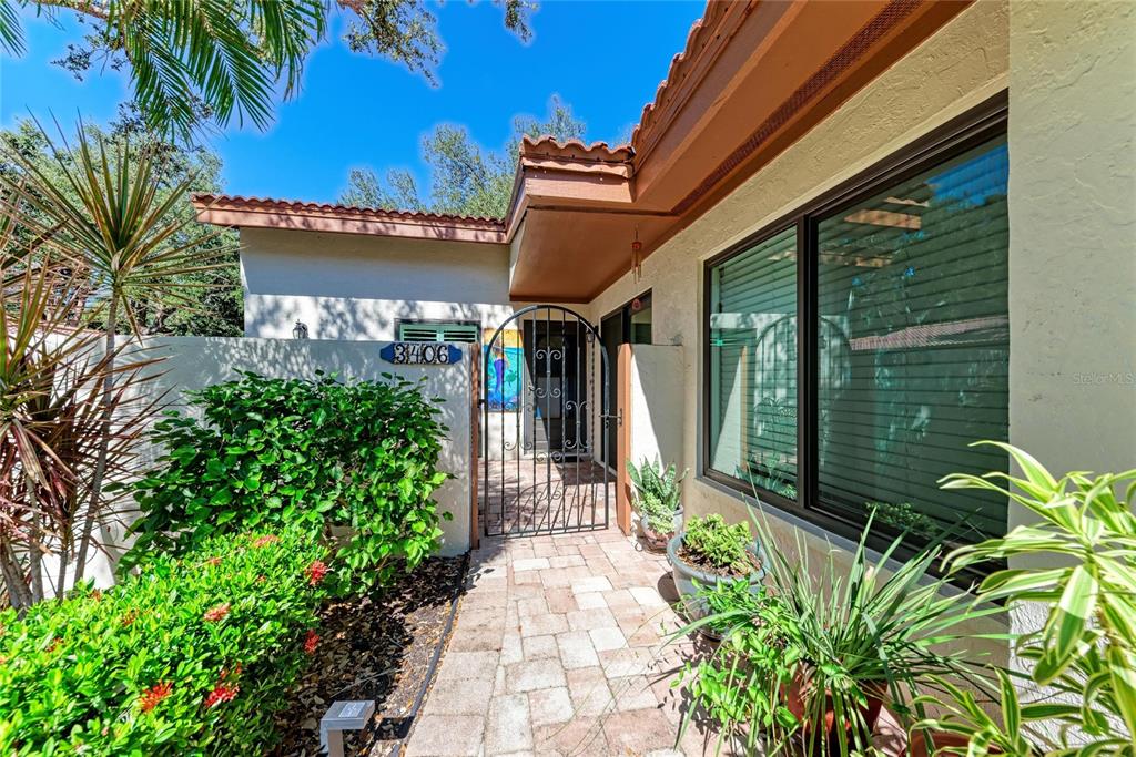 A paved walkway leads to a gated courtyard entrance of a house with stucco walls — 3406 FALCON PLACE, BRADENTON, FL