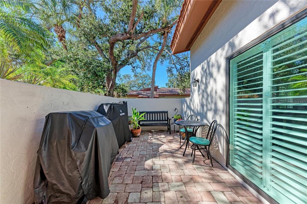 A paved outdoor patio features a covered grill, a small table with chairs, and a bench — 3406 FALCON PLACE, BRADENTON, FL