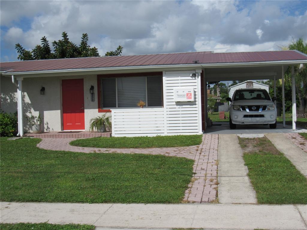 A single-story house with a red door, metal roof, and a carport with a parked car — 6273 SOONER STREET, NORTH PORT, FL