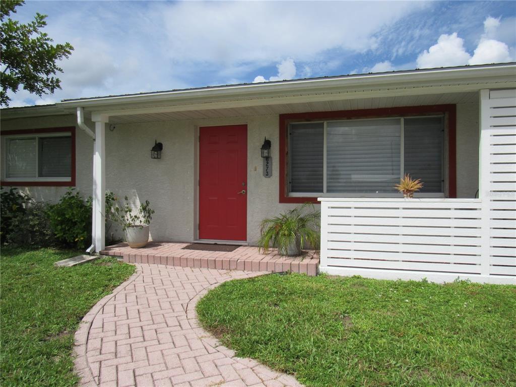 A single-story house exterior features a red front door, brick walkway, and white privacy fence — 6273 SOONER STREET, NORTH PORT, FL