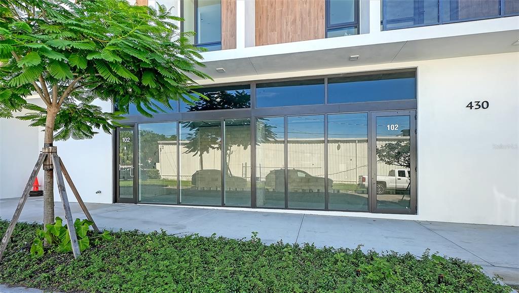 The exterior of a modern commercial building features large glass windows and two glass doors — 430 KUMQUAT COURT UNIT 102, SARASOTA, FL