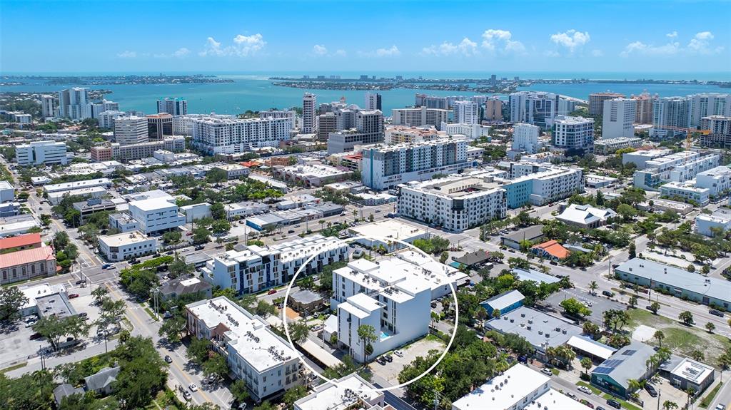 An aerial view shows a white multi-story apartment building circled in a dense urban neighborhood — 430 KUMQUAT COURT UNIT 102, SARASOTA, FL