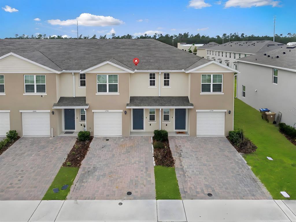 An exterior view of a row of attached townhomes with paved driveways and garages — 2798 BRIE HAMMOCK BEND, HARMONY, FL