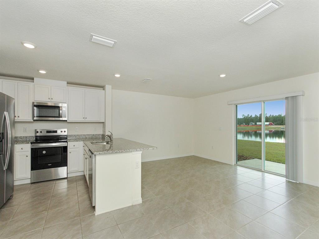 A kitchen with white cabinets and stainless steel appliances opens to a tiled living area — 2798 BRIE HAMMOCK BEND, HARMONY, FL