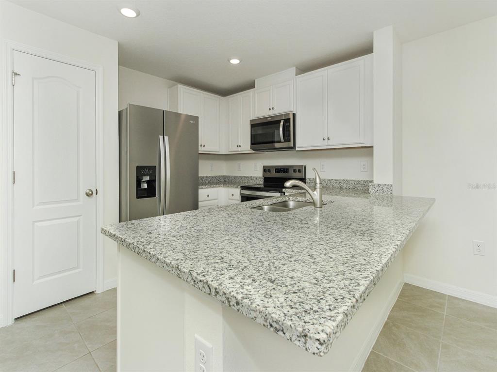 A kitchen features white cabinets, granite countertops, stainless steel appliances, and a breakfast bar — 2798 BRIE HAMMOCK BEND, HARMONY, FL