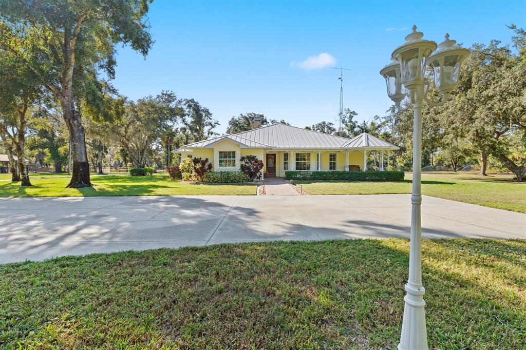 A yellow single-story house with a metal roof sits behind a large concrete driveway — 3971 NE ALBIN AVENUE, NORTH PORT, FL