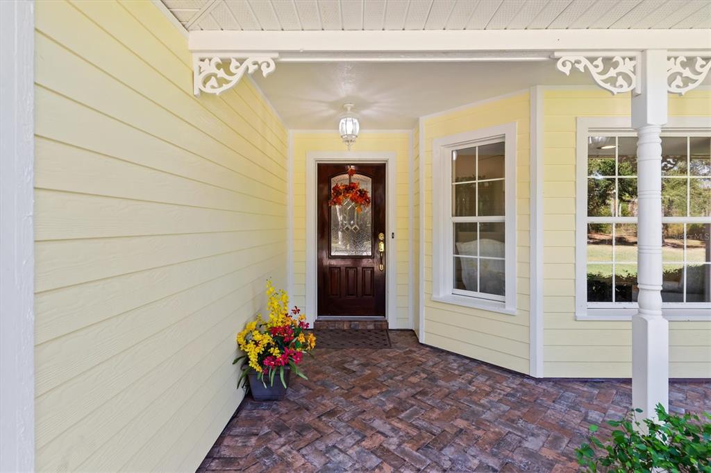 A covered porch with yellow siding, a brick floor, and a dark wood front door — 3971 NE ALBIN AVENUE, NORTH PORT, FL