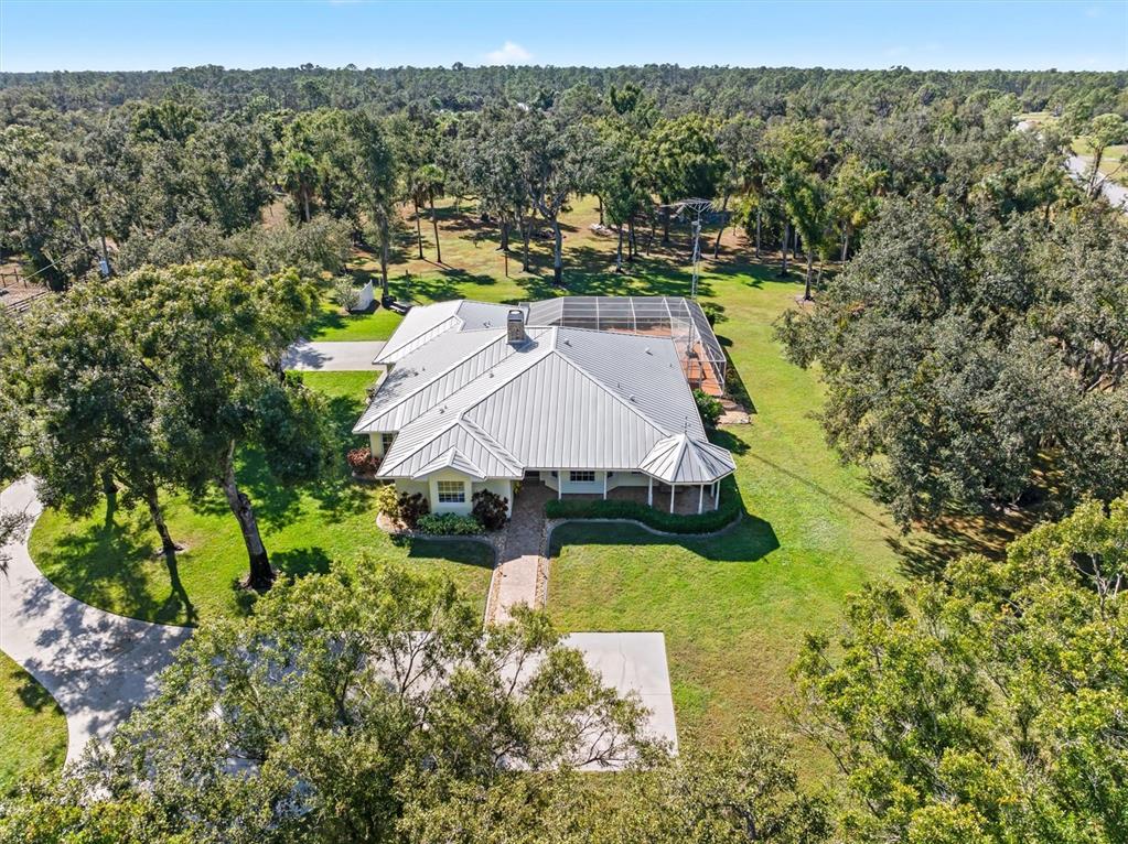 An aerial view shows a single-story house with a metal roof and a screened-in pool — 3971 NE ALBIN AVENUE, NORTH PORT, FL