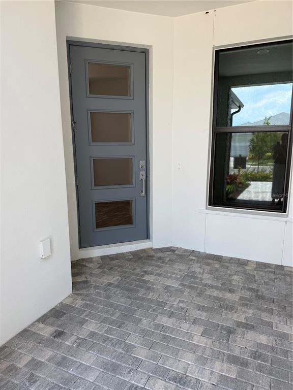 A gray front door with four glass panels sits beside a window on a paved porch — 5853 WINDBREAK COURT, APOLLO BEACH, FL
