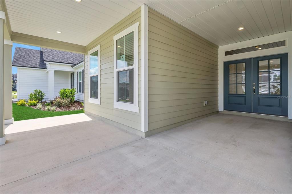 A covered concrete porch features light green siding, white trim, and dark blue double doors — 3453 AMERICANA DRIVE, GREEN COVE SPRINGS, FL