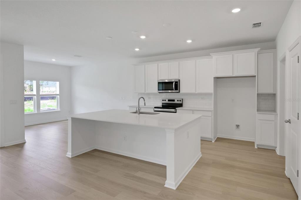 A modern kitchen features white cabinets, a large island with a sink, and light wood flooring — 3453 AMERICANA DRIVE, GREEN COVE SPRINGS, FL