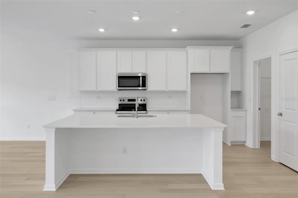 A modern kitchen features white cabinetry, a large central island, and light wood flooring — 3453 AMERICANA DRIVE, GREEN COVE SPRINGS, FL