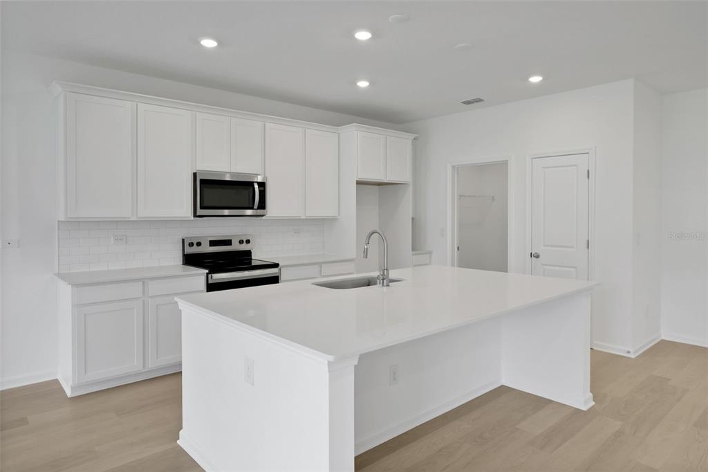 A modern kitchen features white cabinets, a large quartz island, and stainless steel appliances — 3453 AMERICANA DRIVE, GREEN COVE SPRINGS, FL