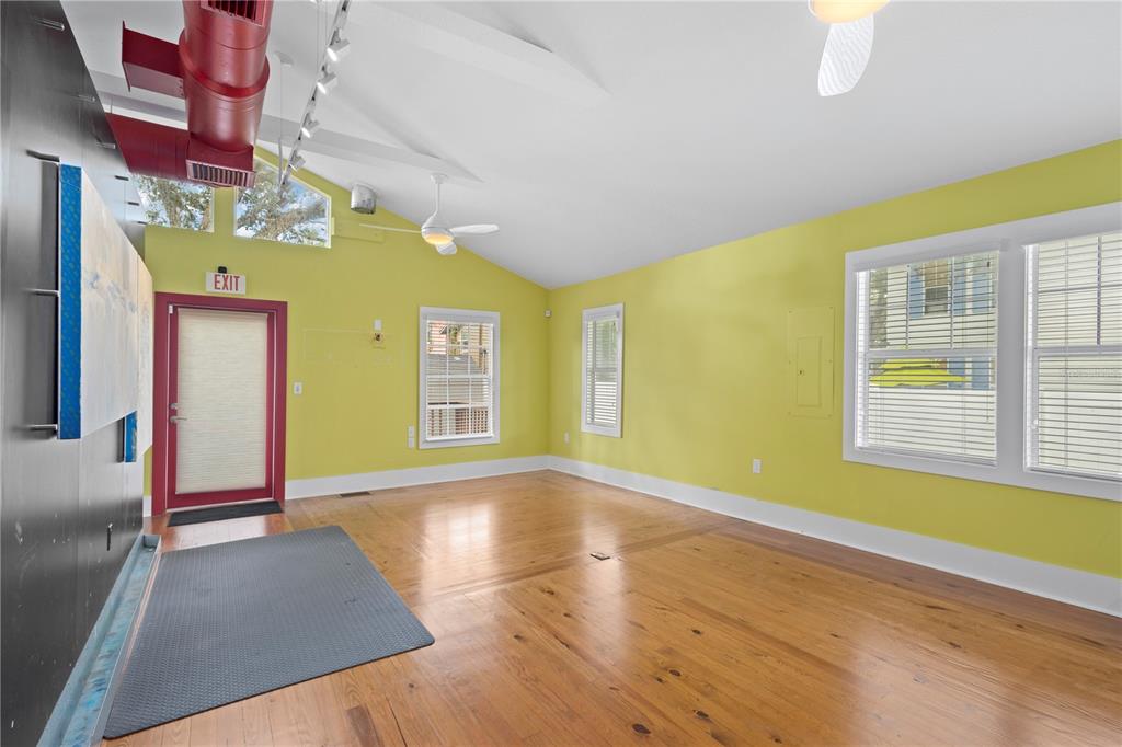 A room with lime green walls, hardwood floors, exposed red ductwork, and an exit door — 1950 ADAMS LANE, SARASOTA, FL