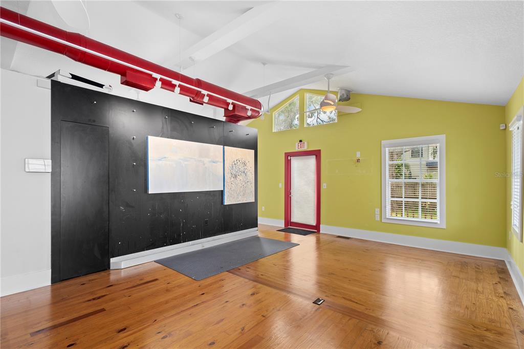 A room with hardwood floors, a black accent wall, and exposed red industrial ceiling pipes — 1950 ADAMS LANE, SARASOTA, FL