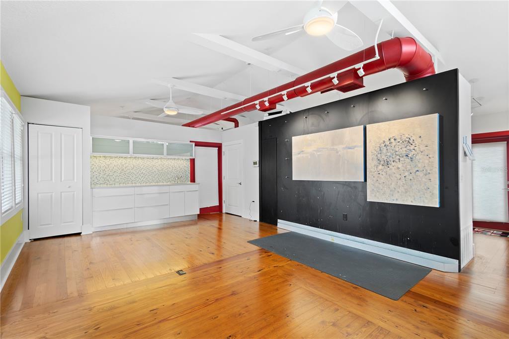 A room with hardwood floors, a white kitchenette, and a large black wall with art — 1950 ADAMS LANE, SARASOTA, FL