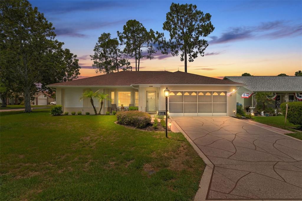 A single-story house with a patterned concrete driveway and a two-car garage at dusk — 7196 CROWN OAKS DRIVE, SPRING HILL, FL