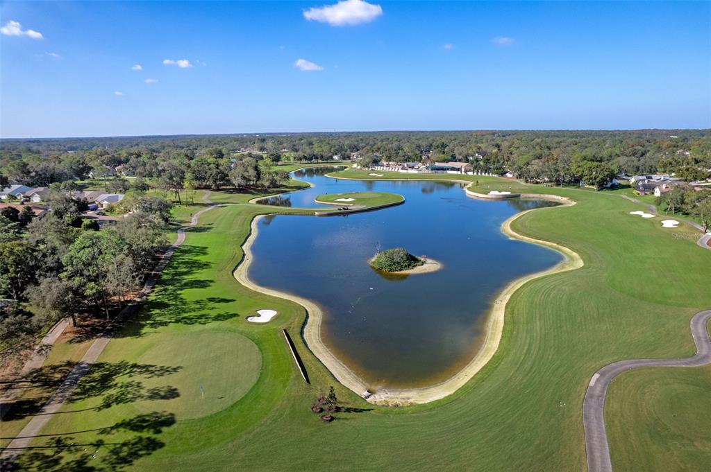 An aerial view of a golf course featuring a large pond with a small island — 7196 CROWN OAKS DRIVE, SPRING HILL, FL