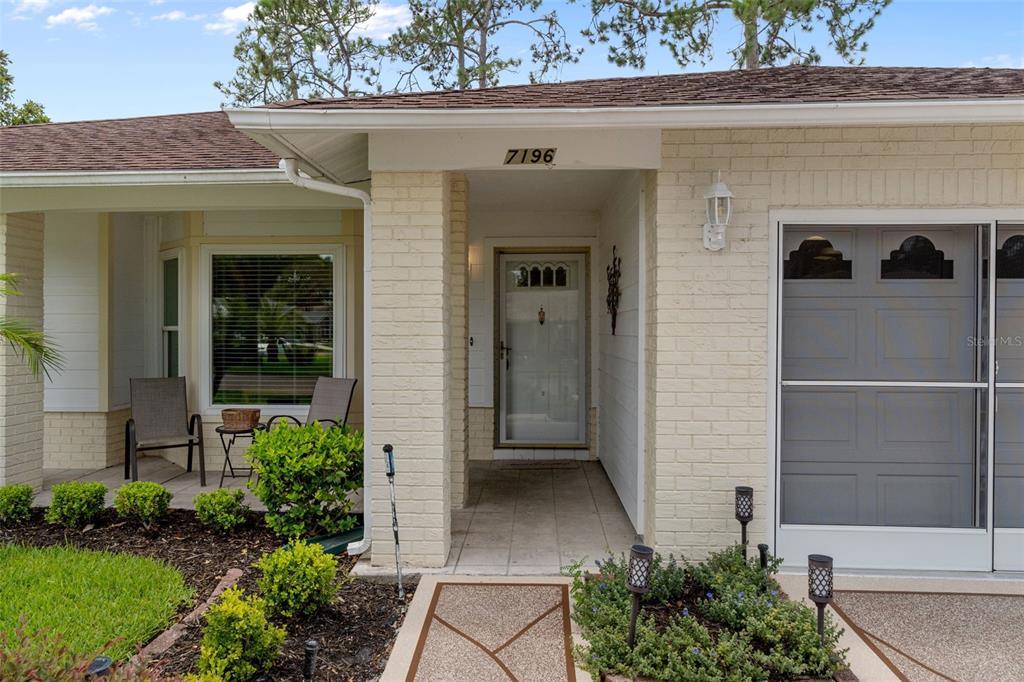 The exterior of a light-colored brick house features a covered entryway and a garage door — 7196 CROWN OAKS DRIVE, SPRING HILL, FL