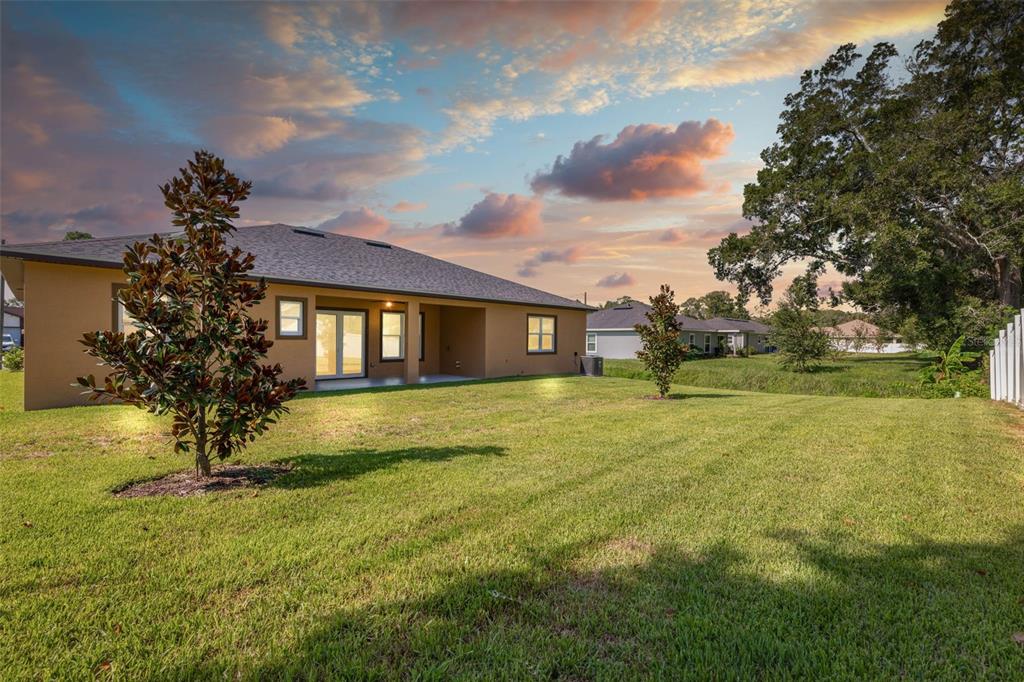 The backyard of a tan house features a grassy lawn, two small trees, and sunset — 57 FLAMINGO DRIVE, PALM COAST, FL