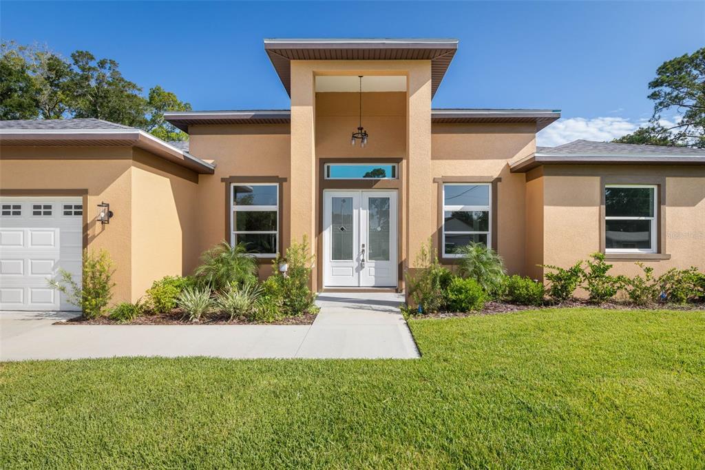 A tan single-story house with a double front door, a garage, and a grassy lawn — 57 FLAMINGO DRIVE, PALM COAST, FL
