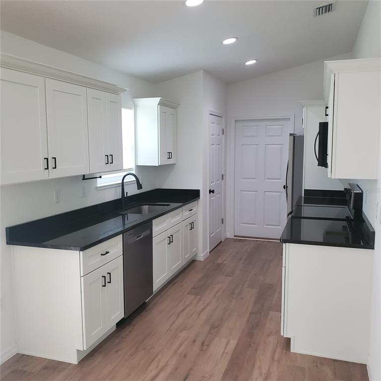 A kitchen with white cabinets, black countertops, stainless steel appliances, and light wood-look flooring — 353 FISHER WAY, OCKLAWAHA, FL