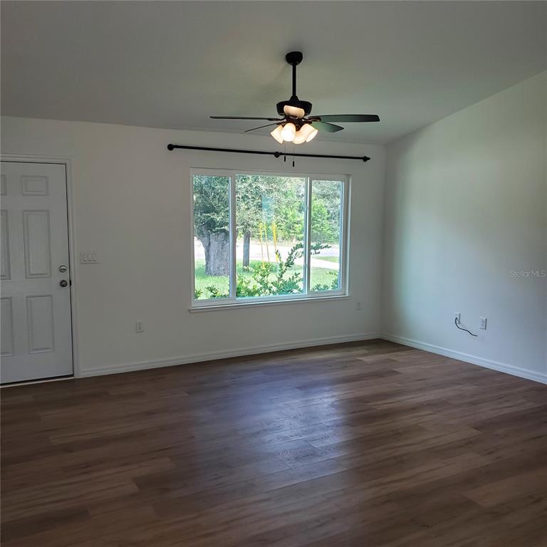 An empty living room features white walls, wood-look flooring, a ceiling fan, and a large window — 353 FISHER WAY, OCKLAWAHA, FL