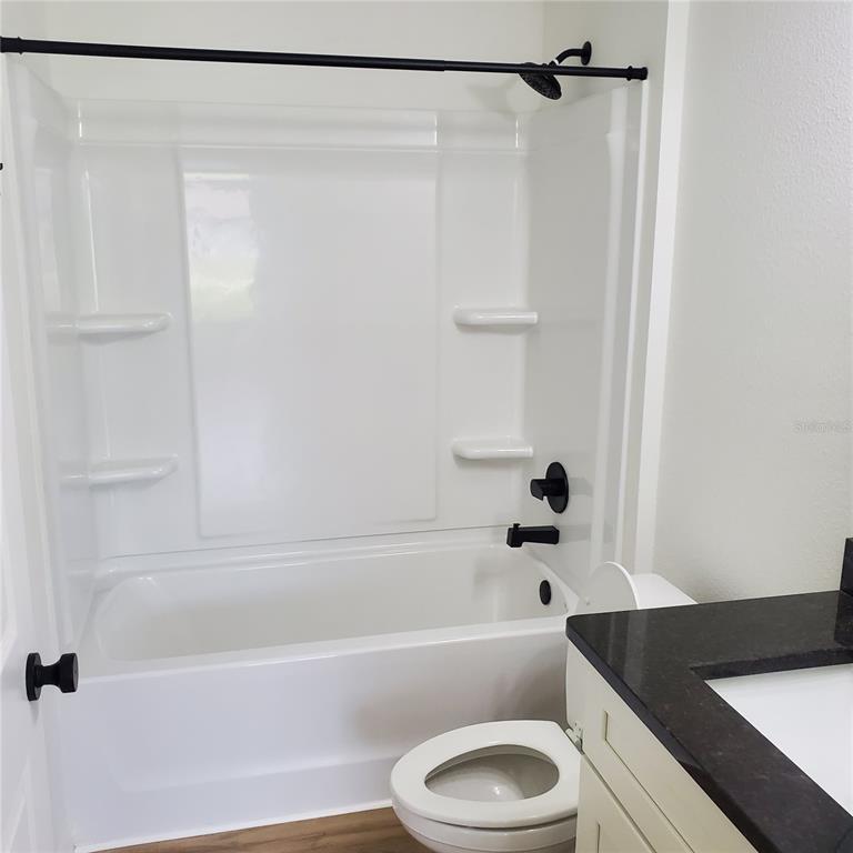 A bathroom features a white tub-shower combo, a toilet, and a vanity with dark countertops — 353 FISHER WAY, OCKLAWAHA, FL