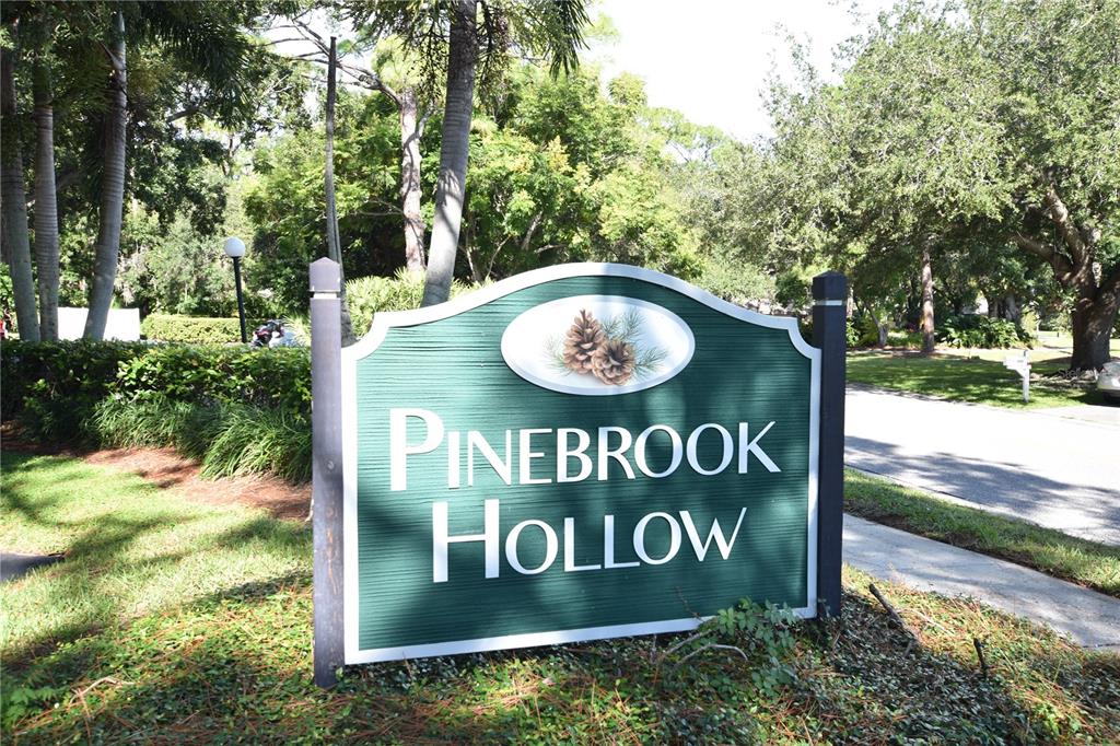 A green sign with the words Pinebrook Hollow stands in a grassy, tree-lined area — 4610 RINGWOOD MEADOW UNIT 17, SARASOTA, FL