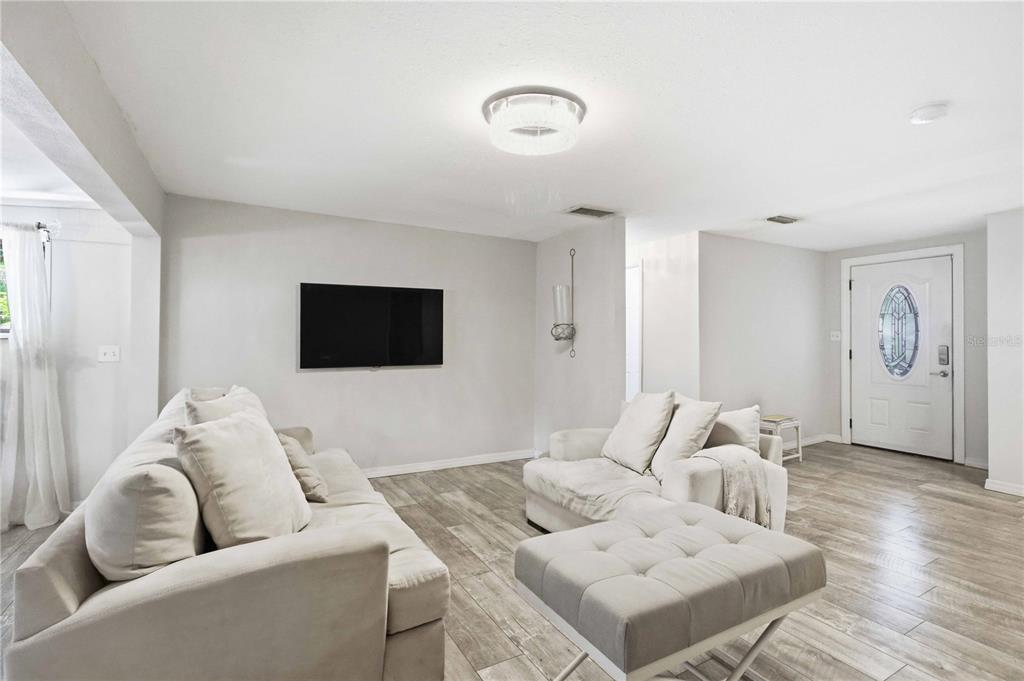 A living room features light wood-look tile flooring, a white sofa, and a wall-mounted television — 603 60TH AVENUE W, BRADENTON, FL