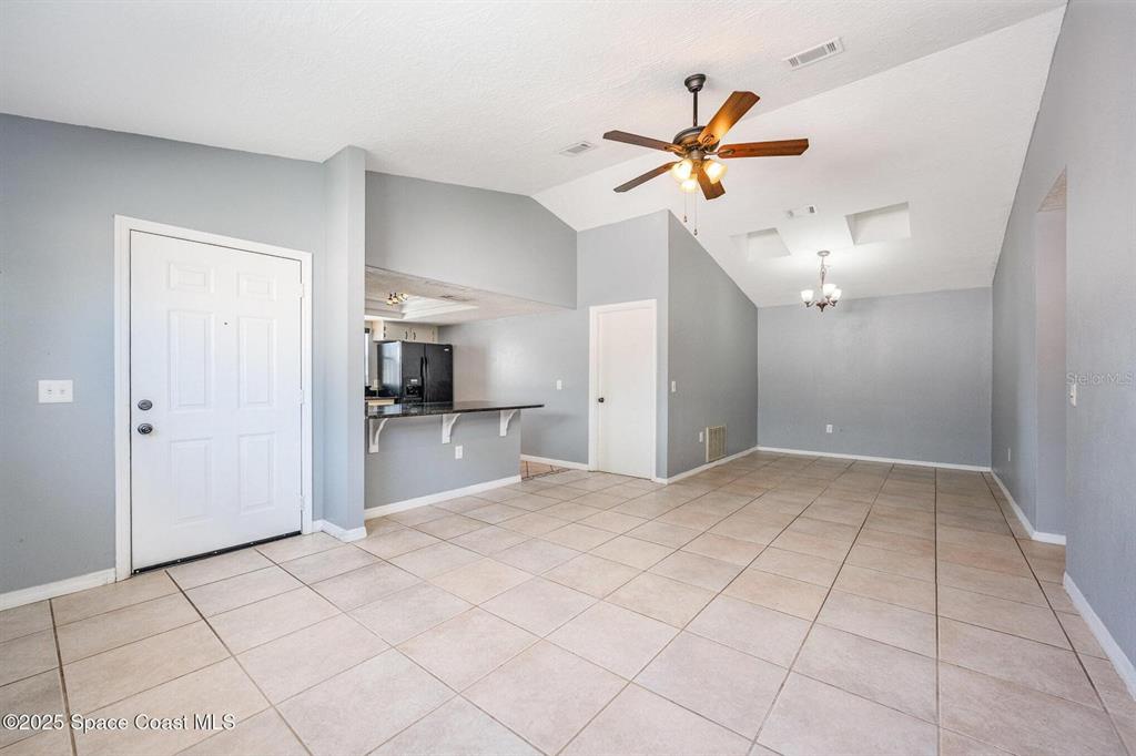 An open-concept living and dining area features vaulted ceilings, tile flooring, and a kitchen pass-through — 4006 DEWBERRY CIRCLE, MELBOURNE, FL
