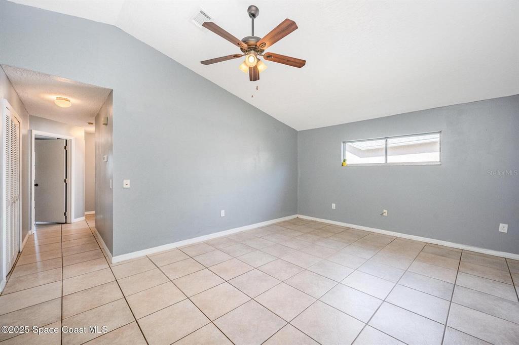 An empty room features gray walls, a vaulted ceiling with a fan, and tiled flooring — 4006 DEWBERRY CIRCLE, MELBOURNE, FL