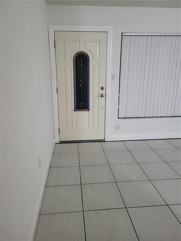 A room with white walls, light-colored tile flooring, a front door, and vertical window blinds — 10803 N ARMENIA AVENUE, TAMPA, FL