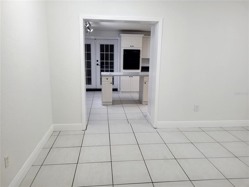 A white-tiled room leads through a doorway into a kitchen with white cabinets and appliances — 10803 N ARMENIA AVENUE, TAMPA, FL
