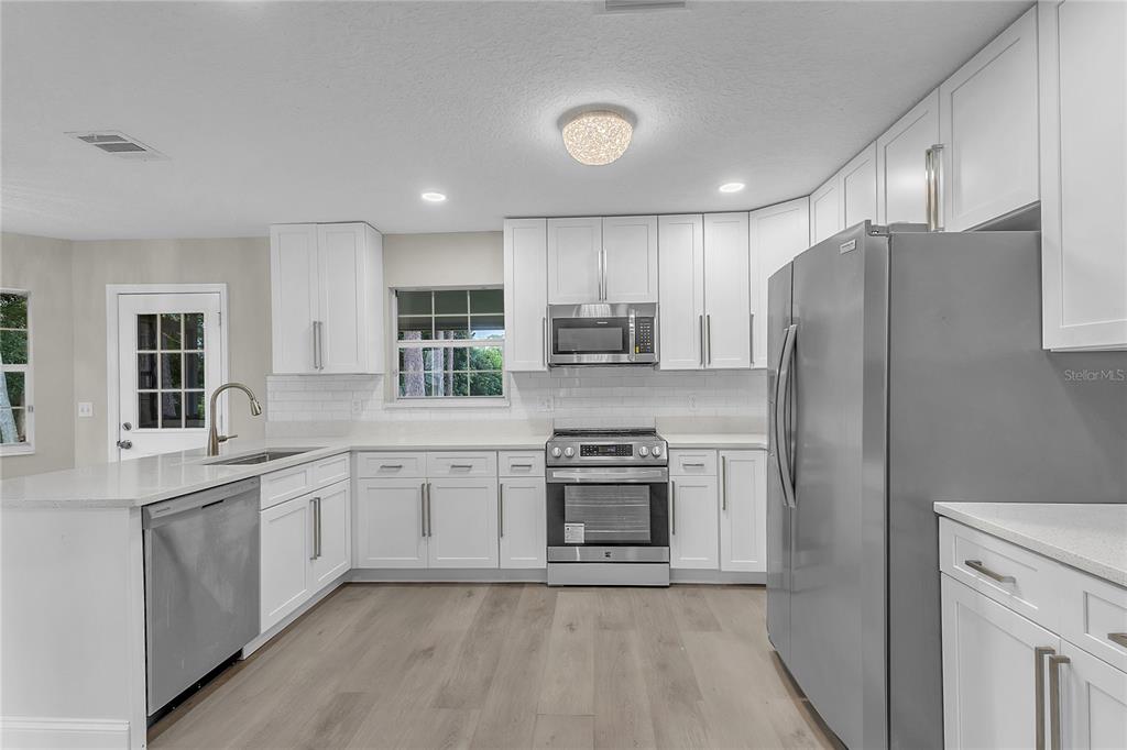 A modern kitchen features white cabinets, stainless steel appliances, and light wood-look flooring — 22 WEIDNER PLACE, PALM COAST, FL