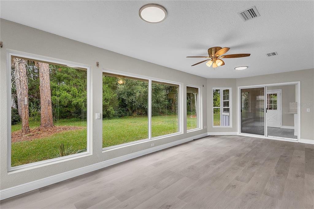 A sunroom with light wood-look flooring, a ceiling fan, and large windows overlooking a yard — 22 WEIDNER PLACE, PALM COAST, FL