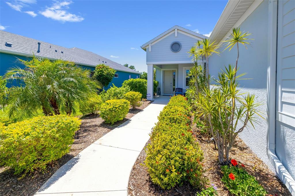 A concrete walkway leads to the front entrance of a light blue house with landscaping — 13638 OLD CREEK CT, PARRISH, FL