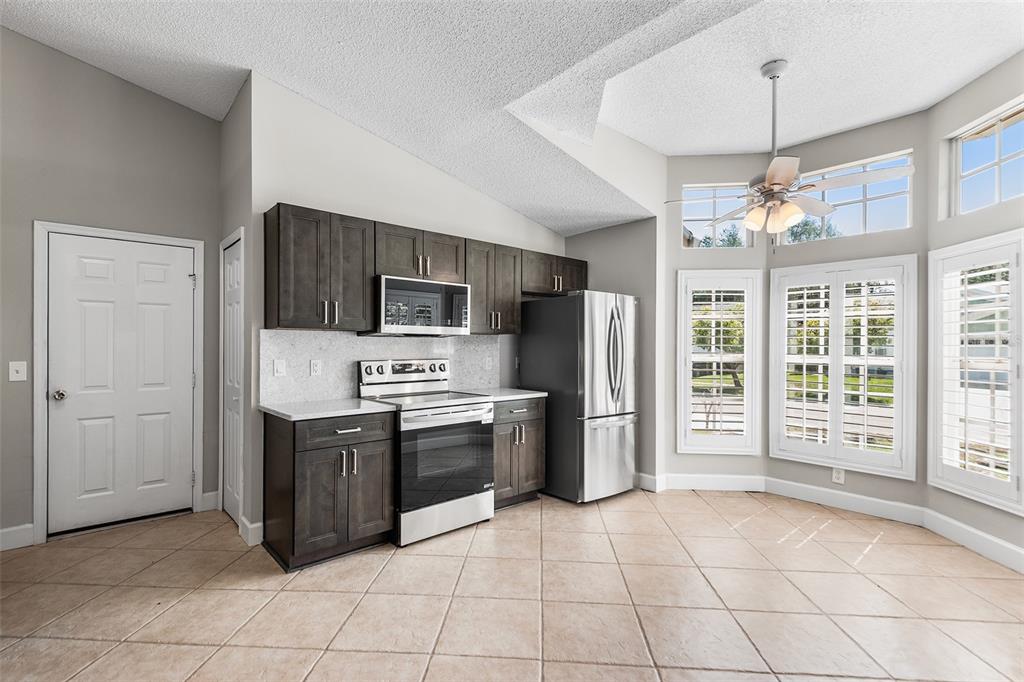 A kitchen features dark wood cabinets, stainless steel appliances, and tile flooring under a vaulted ceiling — 4011 LEVONSHIRE PLACE, VALRICO, FL